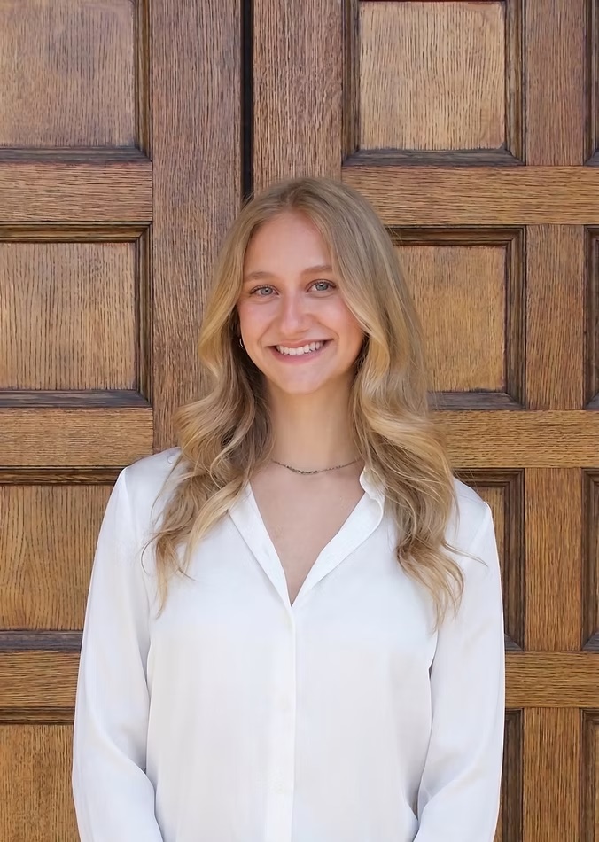 Miriam, a certified health and wellness coach, smiling in front of a wooden door